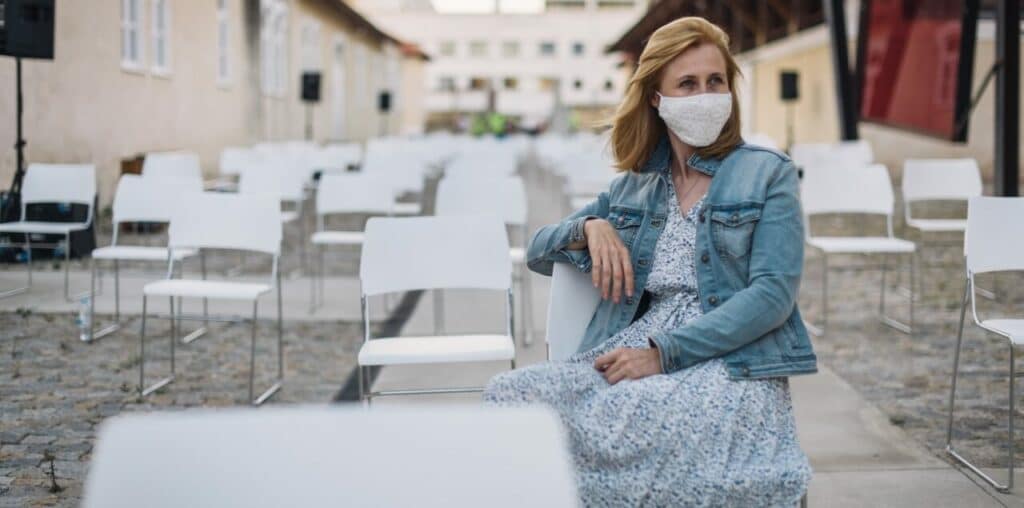 Eine Frau mit Mund-Nasen-Schutz sitzt alleine an einem leeren Veranstaltungsort