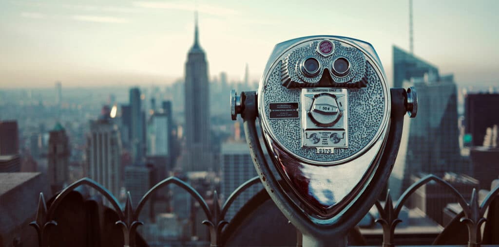 Die Skyline von New York City mit einem Münzfernrohr im Vordergrund als Metapher für Geocodierung
